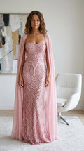 Front view of woman wearing a dusty pink strapless sequin evening gown with a flowing sheer cape