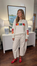 Front full view of woman wearing white Ho Ho Ho Christmas crewneck sweater with wide-leg pants