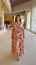 Front full view of woman wearing rust orange and white leaf print halter ruffle maxi dress