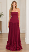 Front view of model wearing burgundy strapless corset maxi dress with pleated skirt and 3D floral hem