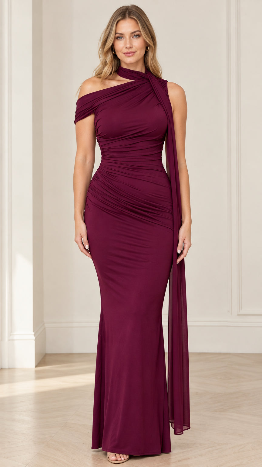 Front view of woman wearing burgundy asymmetric ruched mermaid evening gown with shoulder scarf