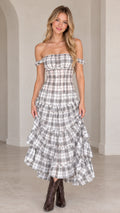 Front view of model wearing grey plaid off-the-shoulder tiered maxi dress with western boots