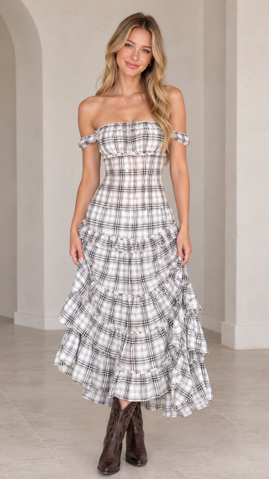 Front view of model wearing grey plaid off-the-shoulder tiered maxi dress with western boots