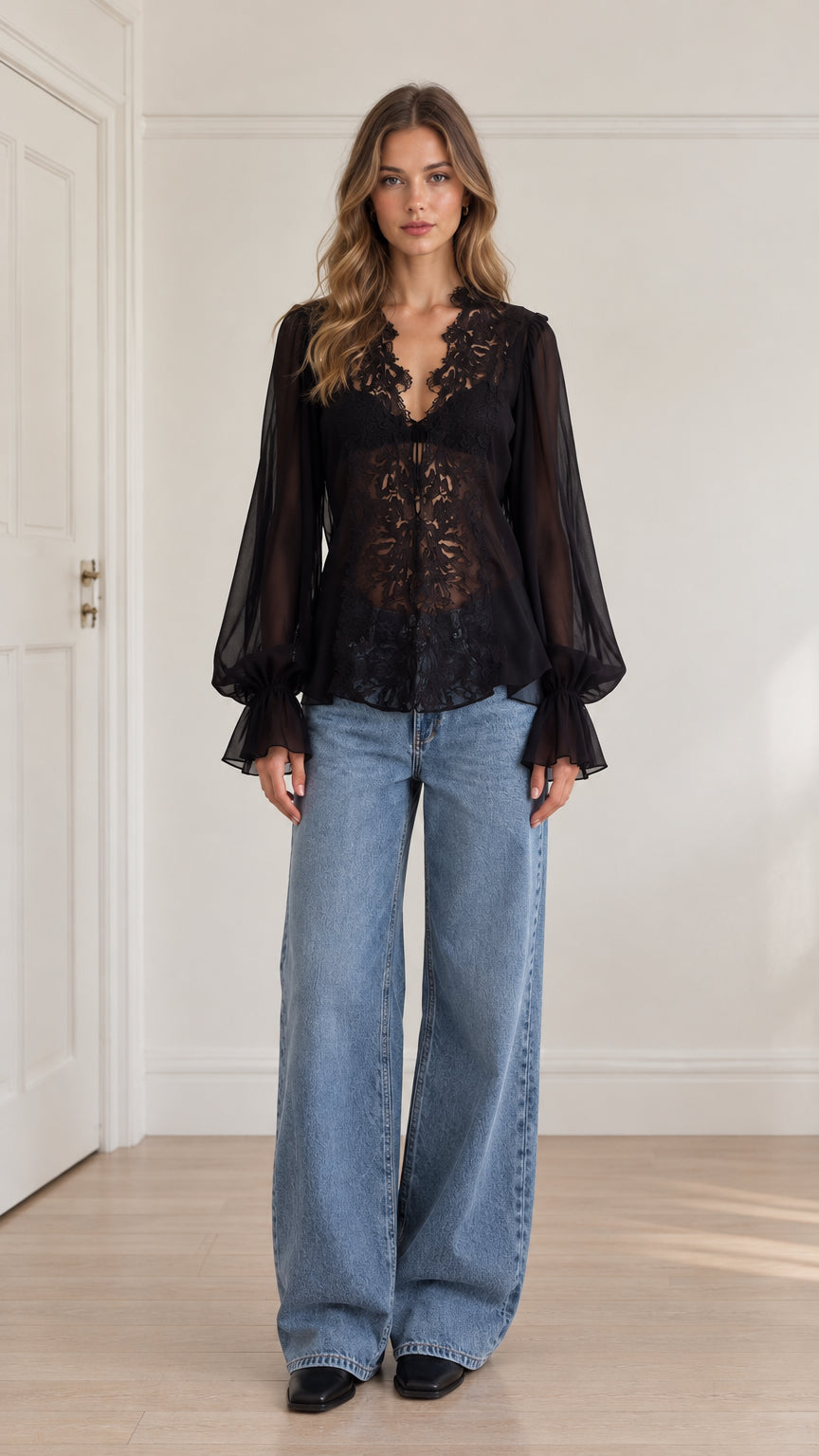 Front view of model wearing black floral lace long sleeve blouse with wide-leg blue jeans