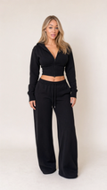 Front view of model wearing black cropped zip hoodie and wide leg sweatpants set