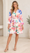 Front view of model wearing white watercolor floral tiered mini dress with smocked waist and long sleeves