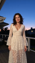 Front view of woman wearing ivory floral lace maxi dress with V-neck and bell sleeves on a balcony
