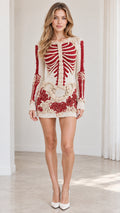 Front view of model wearing cream long sleeve knit mini dress with red embroidered skeleton and roses