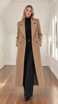 Front full view of a woman wearing a tailored camel maxi overcoat over a black turtleneck and trousers