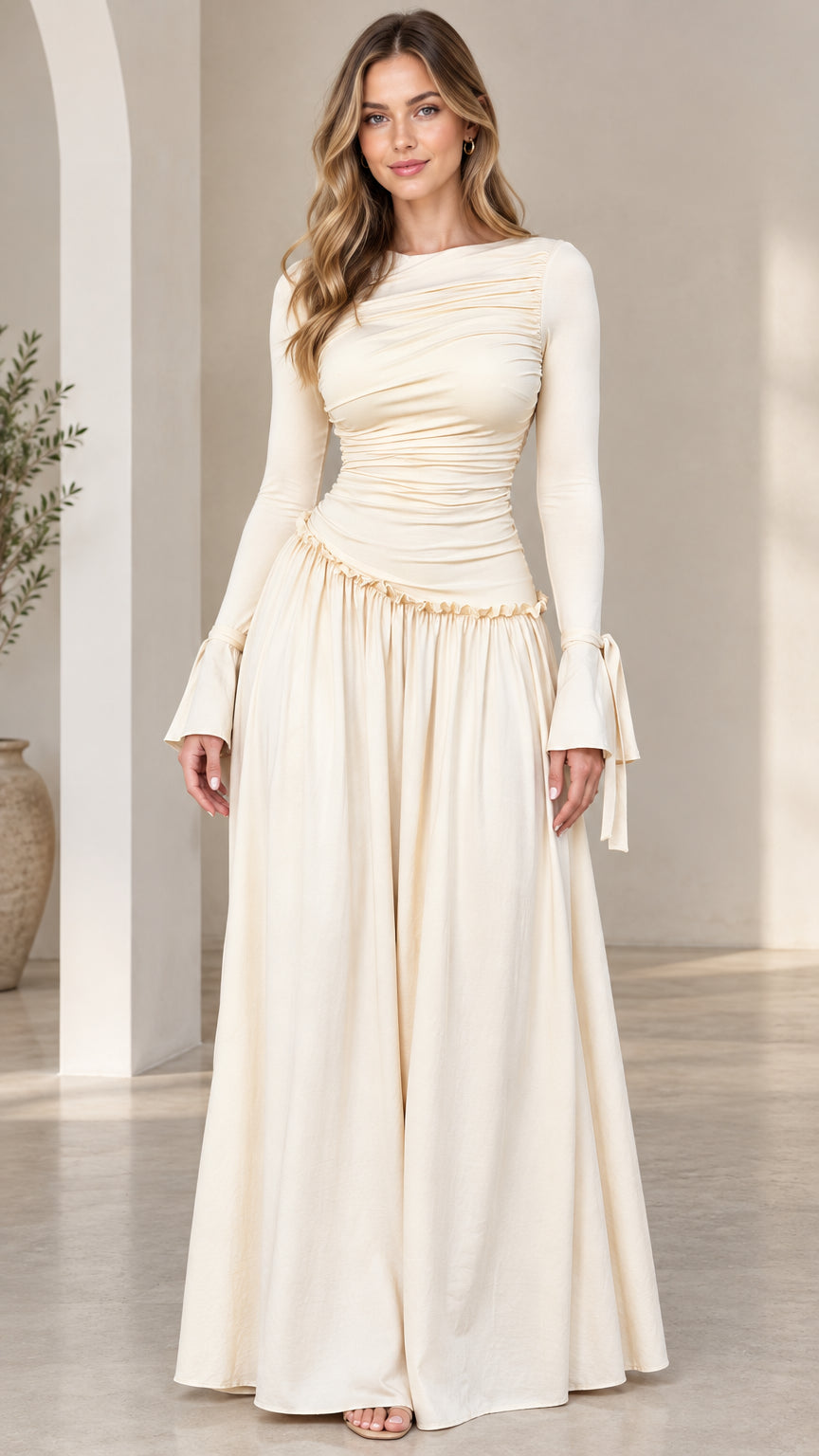 Front full-length view of woman wearing cream ruched drop-waist maxi dress with flared tie cuffs