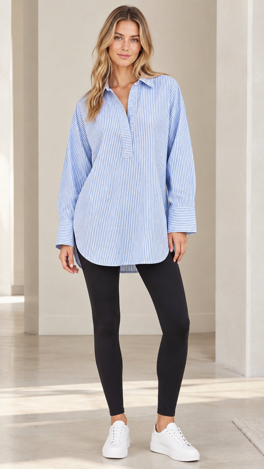 Front full-length view of model wearing light blue striped popover tunic shirt with black leggings