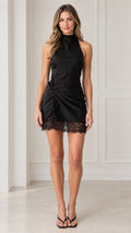 Front view of model wearing black high neck ruched satin mini dress with lace trim