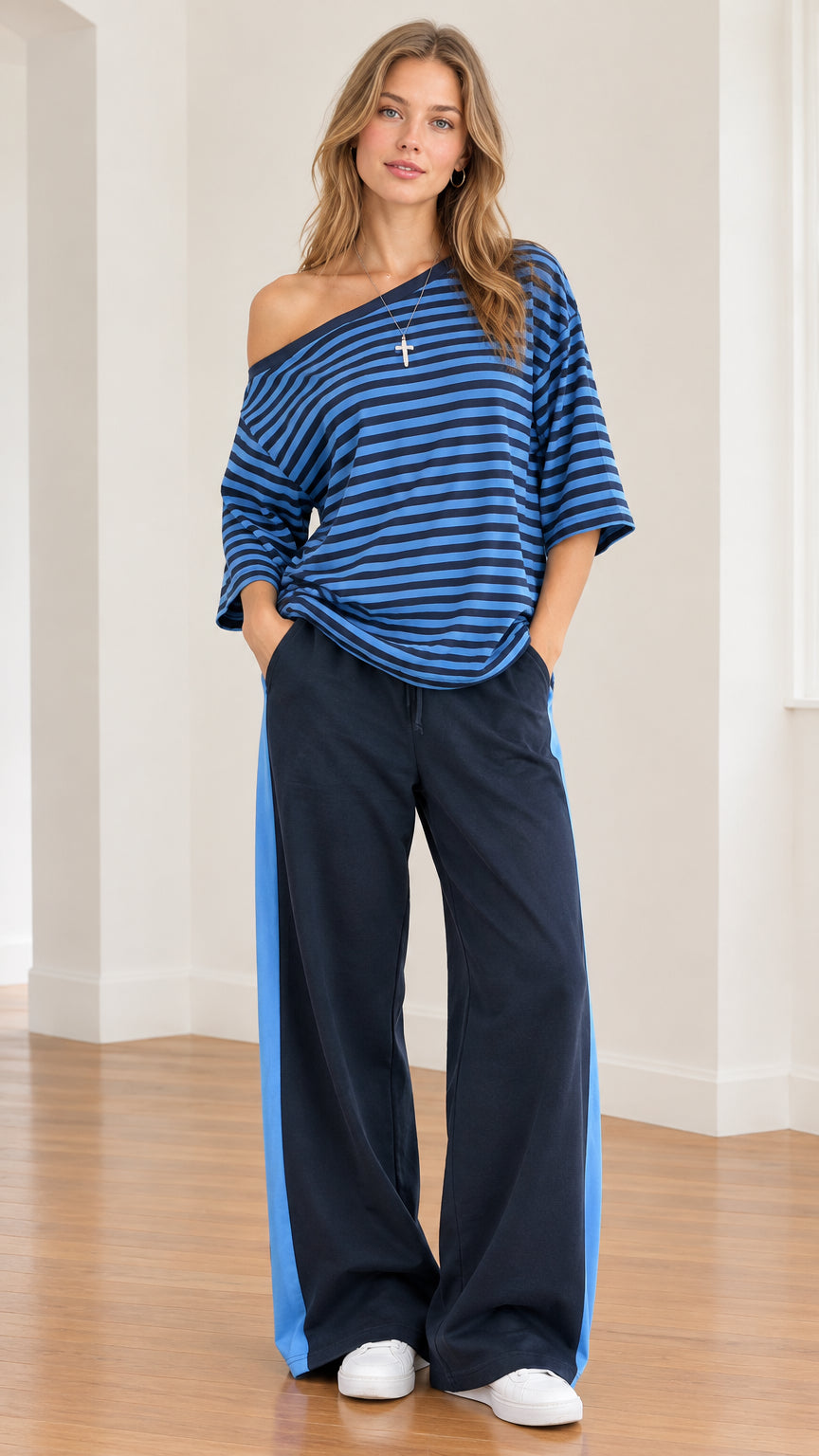 Full front view of model wearing blue striped one-shoulder top with matching side-stripe wide-leg navy pants