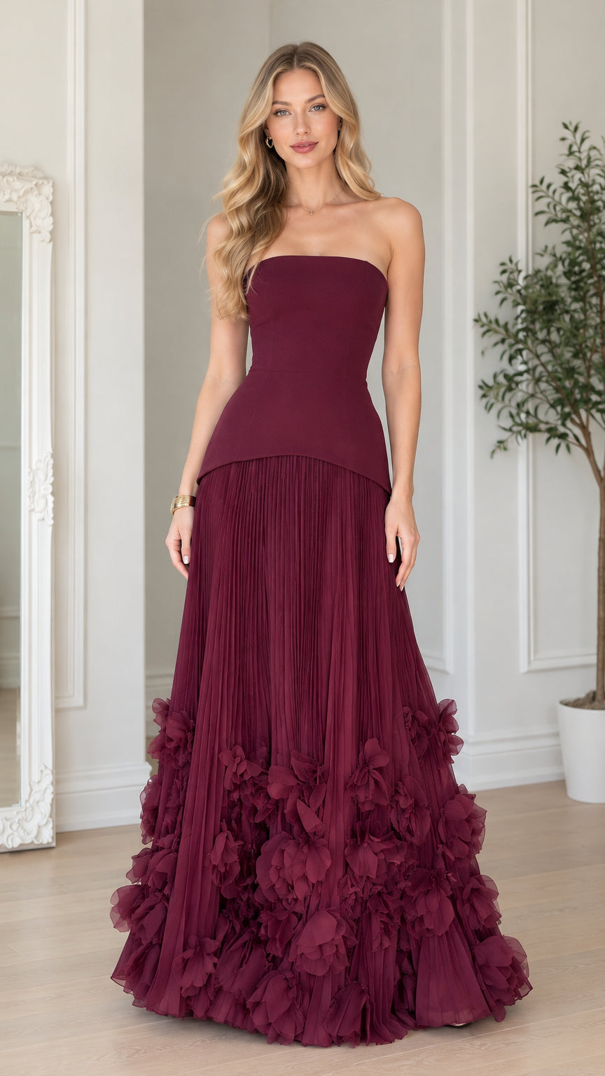Front full-length view of woman wearing strapless burgundy corset pleated gown with 3D floral petal hem