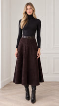 Front full view of woman wearing dark brown suede-look A-line midi skirt with black turtleneck and boots
