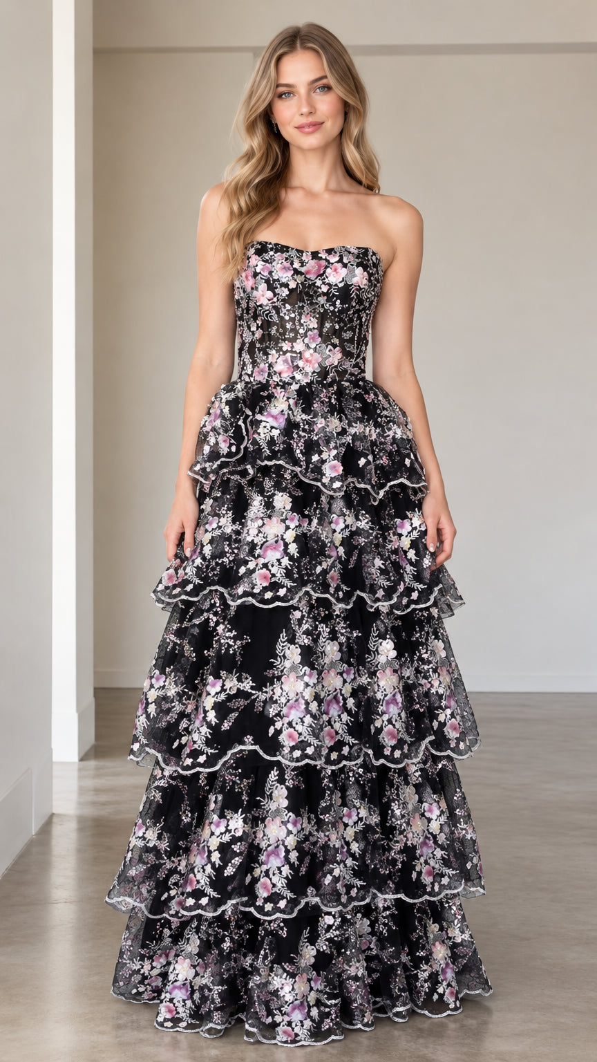 Front full-length view of model wearing black floral embroidered strapless tiered maxi gown