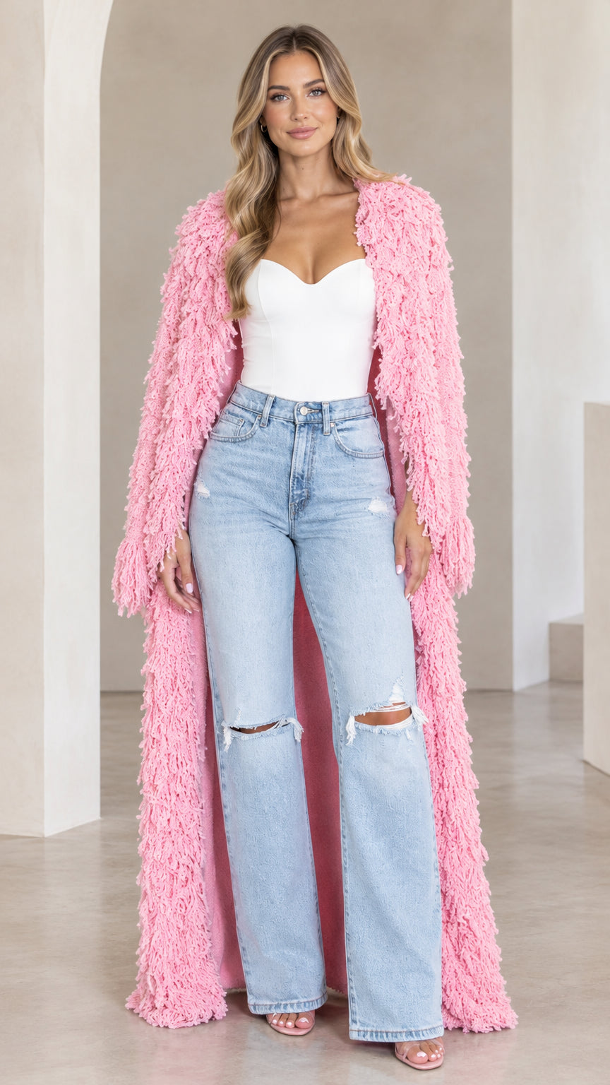 Front view of model wearing pink shaggy knit maxi duster cardigan over corset top and jeans
