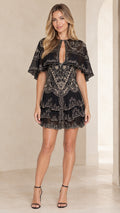 Front full view of woman wearing black embroidered capelet tiered mini dress