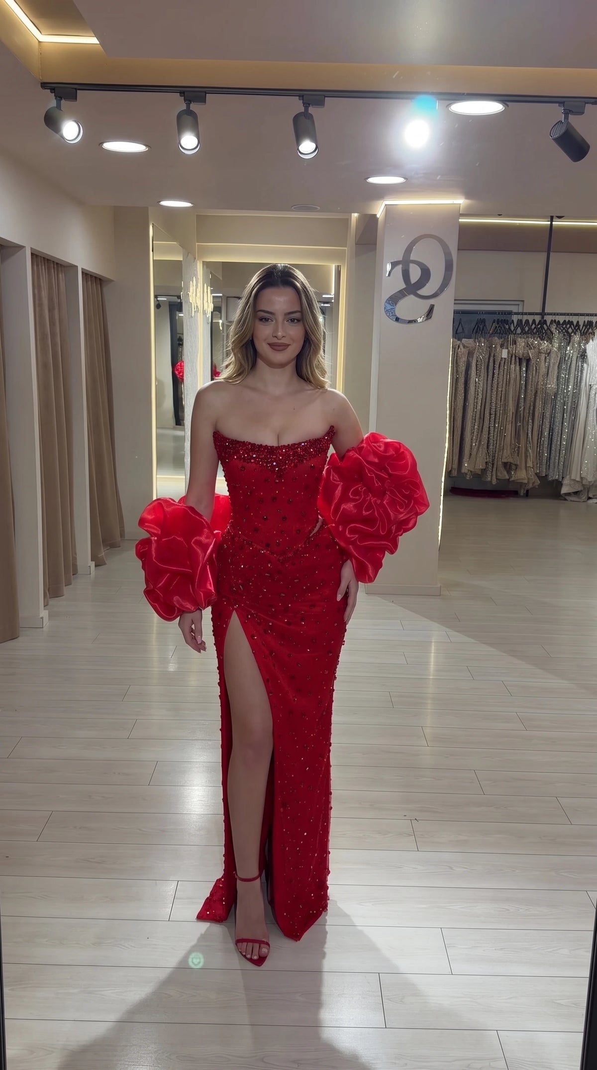 Front view of a red sequin off-shoulder evening gown with voluminous sleeves and side slit
