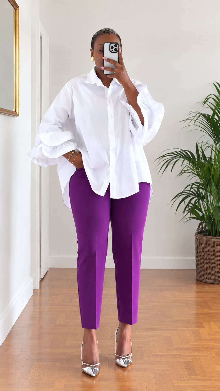 Front full-length view of woman wearing white tiered ruffle sleeve button-down tunic shirt with purple pants
