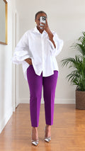 Front full-length view of woman wearing white tiered ruffle sleeve button-down tunic shirt with purple pants