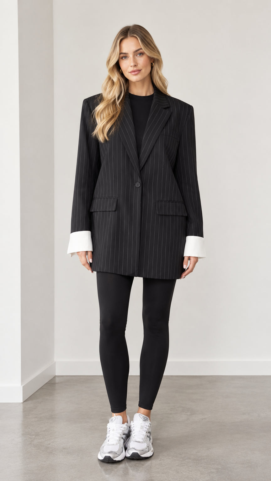 Front full view of woman wearing black oversized pinstripe blazer with contrast white cuffs and leggings