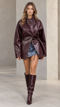 Front full-length view of model wearing burgundy faux leather jacket with cinched drawstring waist and knee-high boots