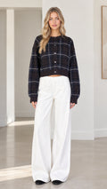 Front full view of woman wearing black plaid cropped cardigan sweater and white wide-leg trousers