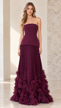 Front view of model wearing burgundy strapless peplum gown with pleated skirt and ruffle hem