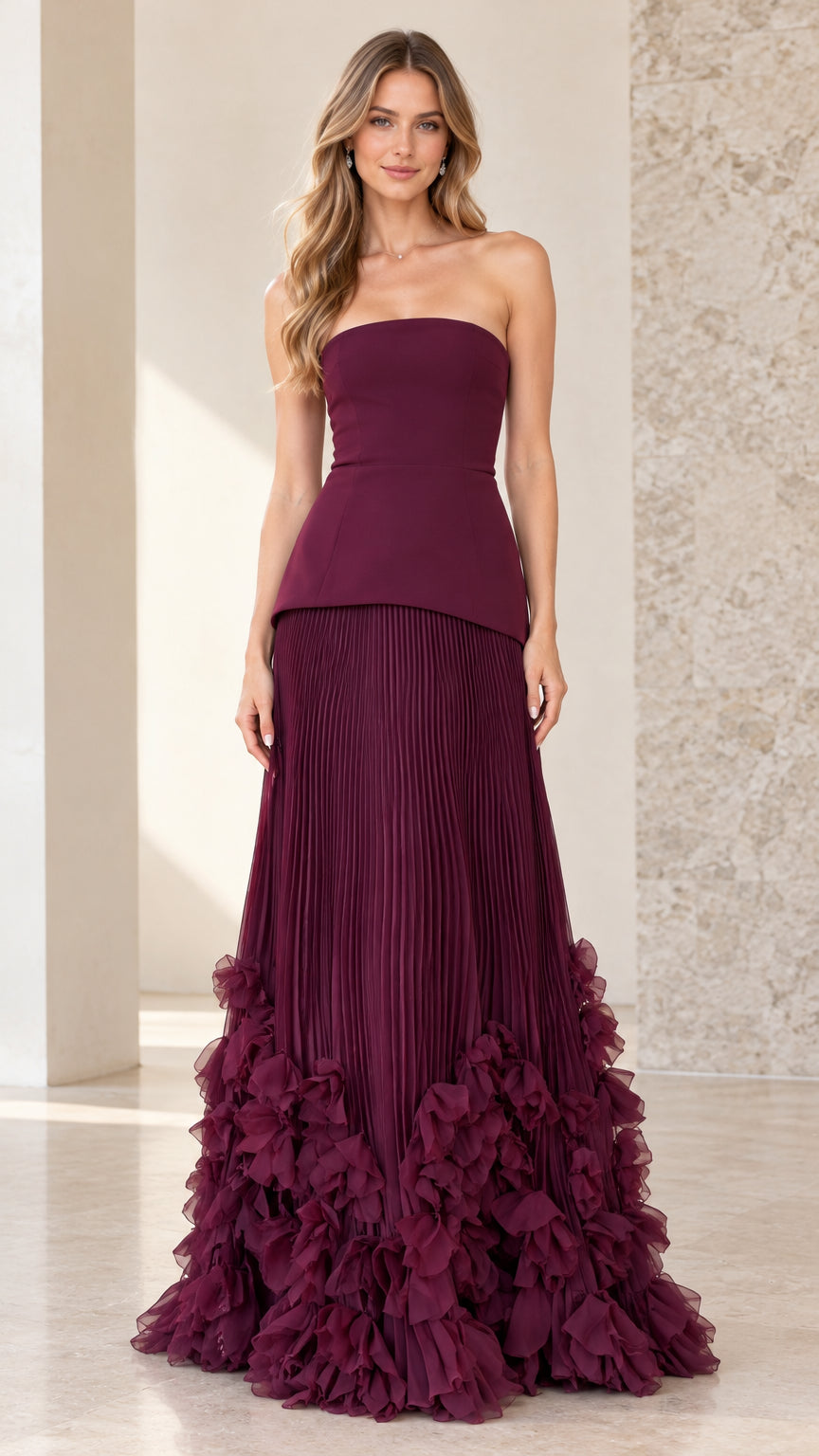 Front view of model wearing burgundy strapless peplum gown with pleated skirt and ruffle hem
