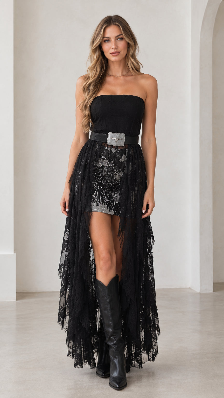 Front view of model wearing black strapless high-low lace maxi dress with western belt and boots