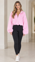 Front view of model wearing pink cropped fleece zip-up jacket with black leggings