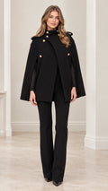 Front full-length view of model wearing black military cape coat with gold buttons and matching black trousers