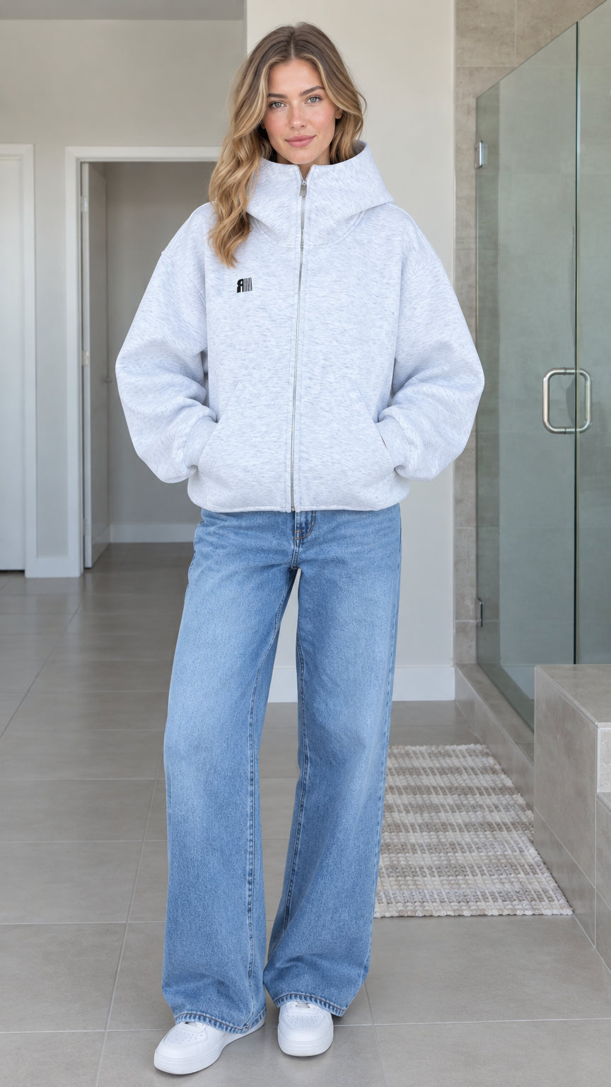 Front full-length view of model wearing heather grey oversized high-neck zip-up fleece hoodie with wide leg jeans