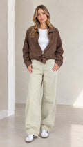 Front full view of woman wearing brown belted zip utility jacket paired with light pants