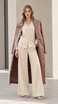 Front view of model wearing a brown longline trench coat with beige button-up shirt and wide-leg trousers