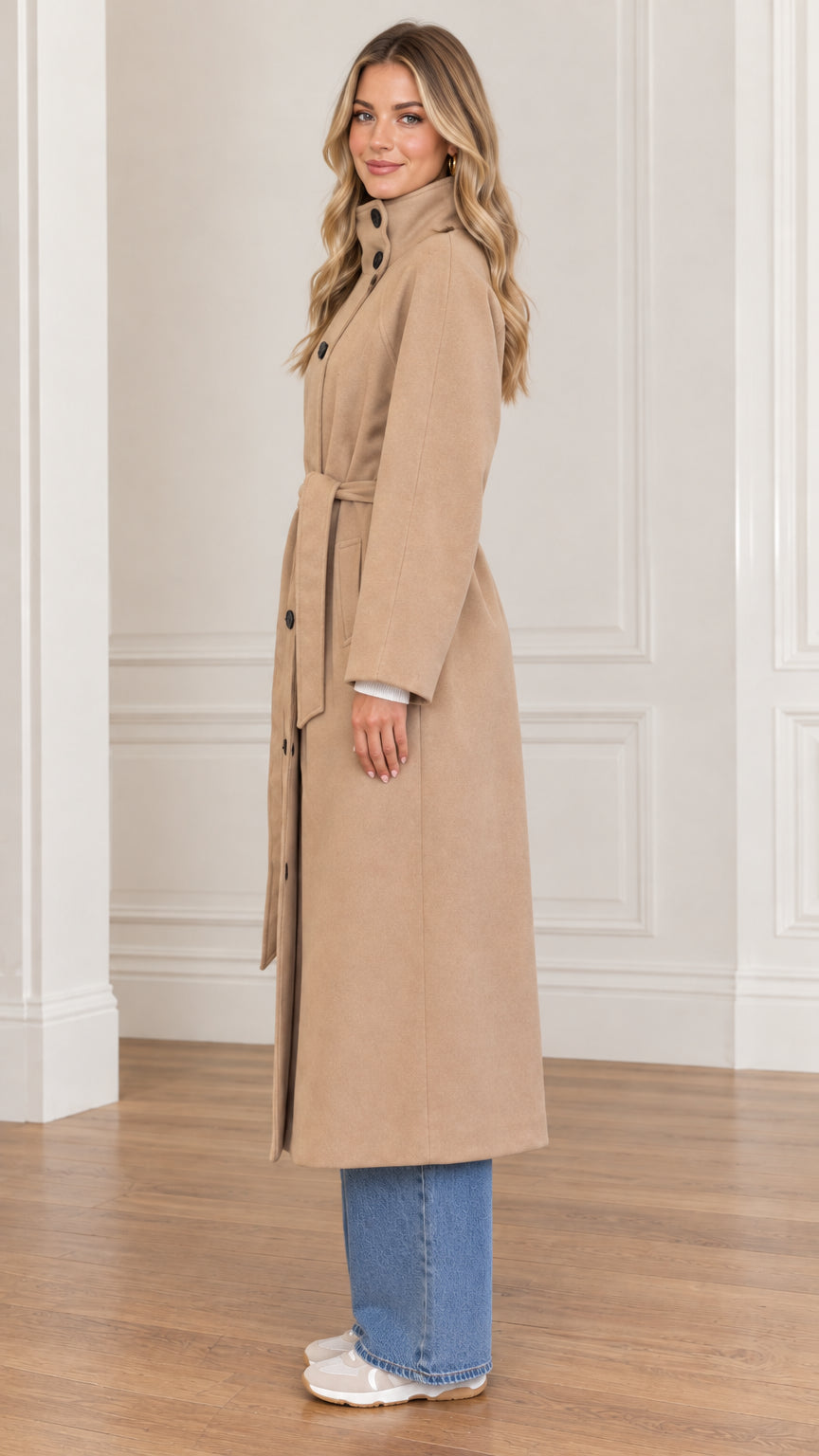 Side profile view of woman modeling camel high neck long coat with waist tie