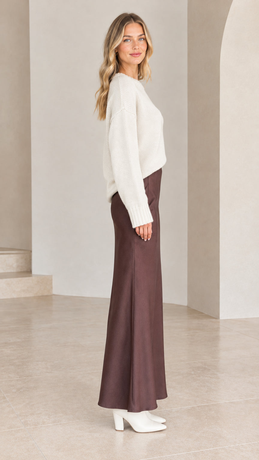 Model wearing white relaxed knit sweater and brown satin skirt - side profile view