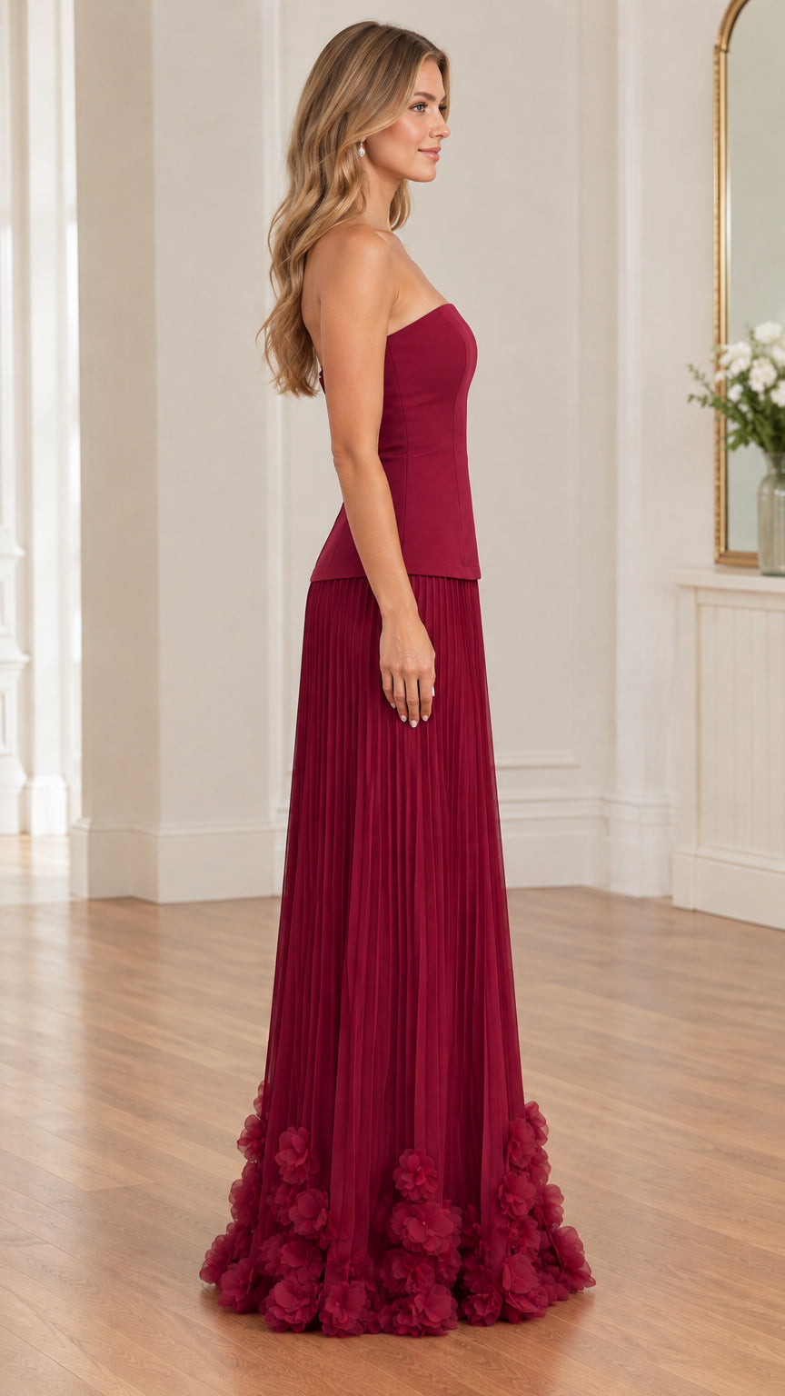 Side profile of model in burgundy strapless evening gown showing pleated skirt and fit