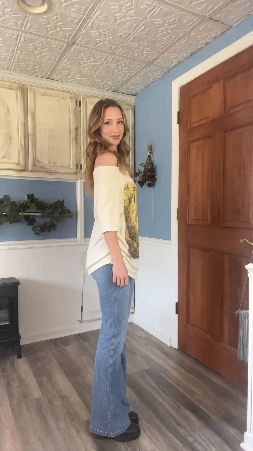Side view of model wearing beige off the shoulder graphic tunic top