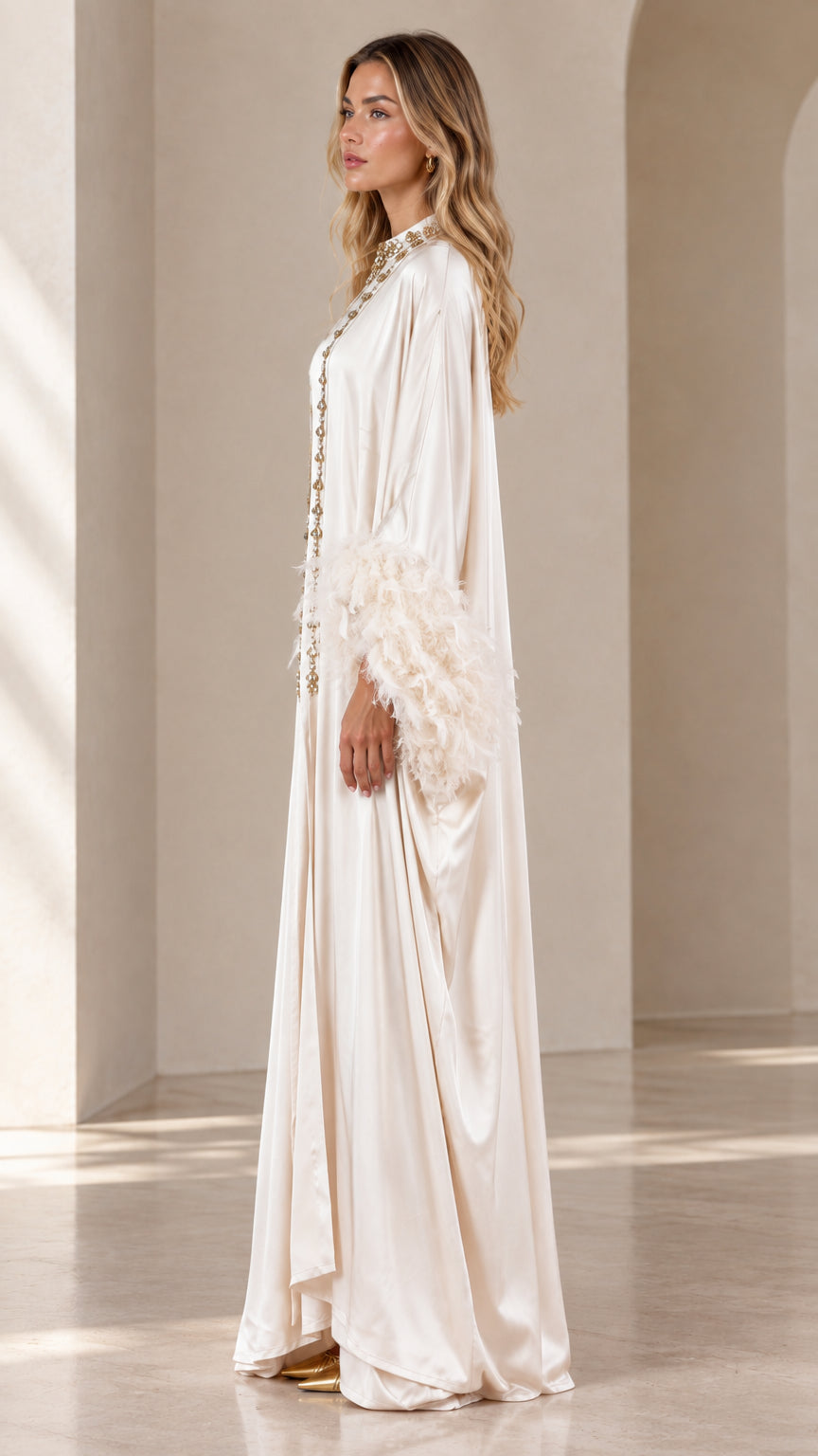 Side angle view of woman wearing champagne satin maxi kaftan with feather trim sleeves