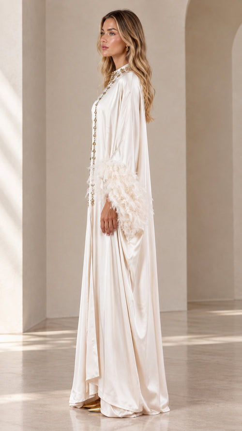 Side angle view of woman wearing champagne satin maxi kaftan with feather trim sleeves