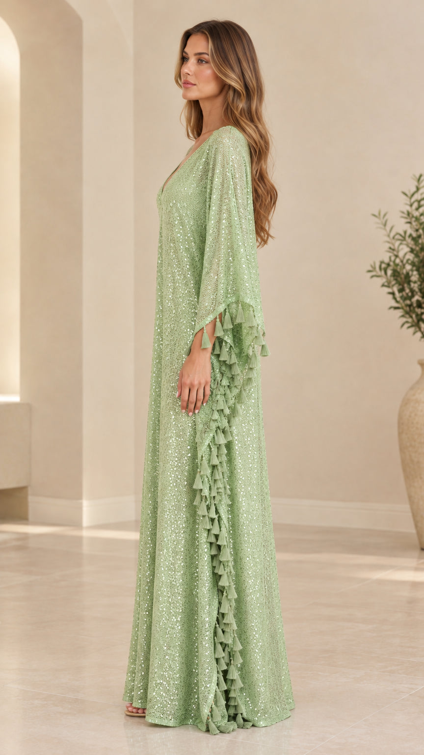 Side profile of woman in flowing sage green sequin kaftan dress showing draped batwing sleeve