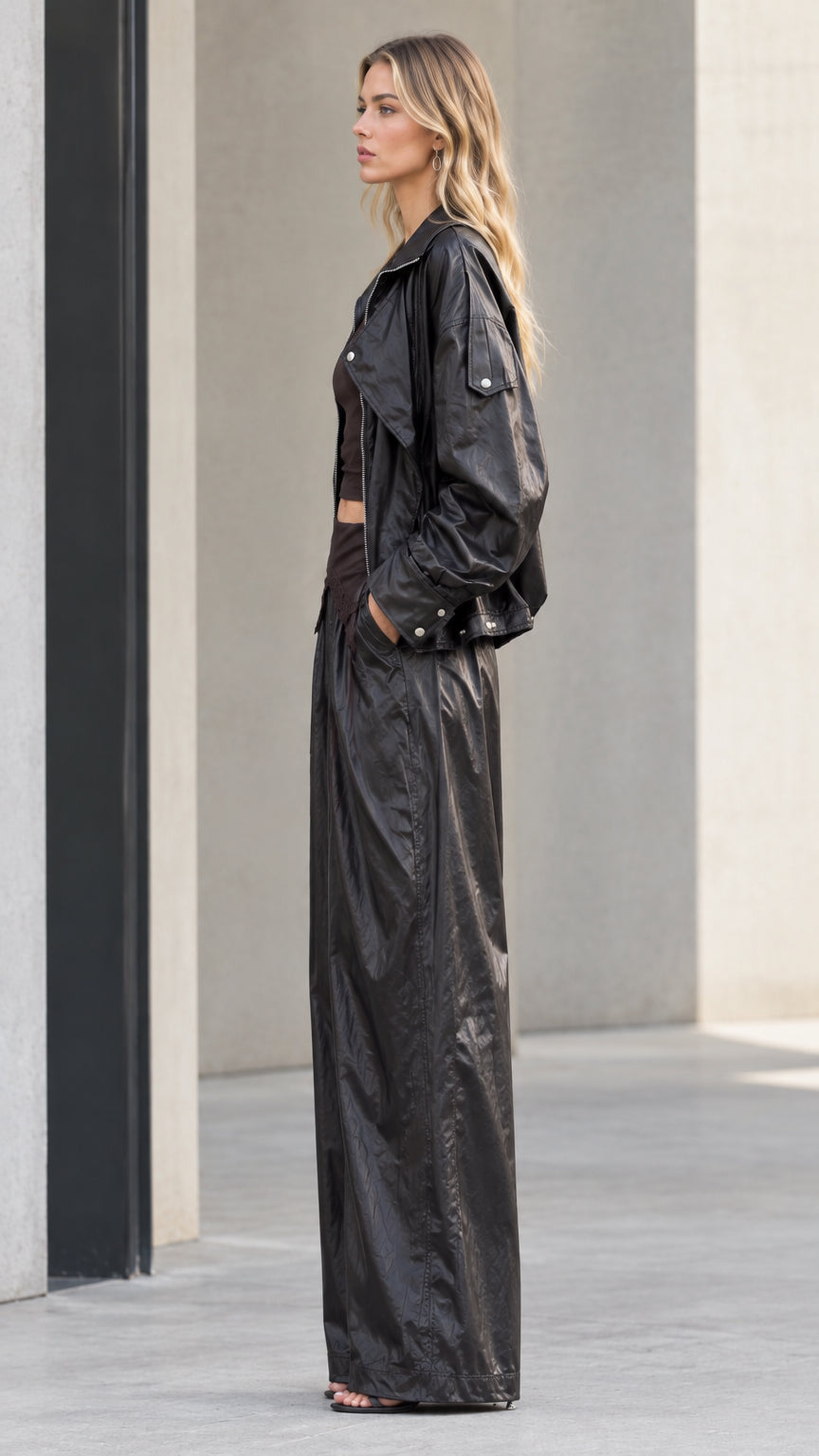 Side profile of model wearing black crinkle metallic jacket and trousers set