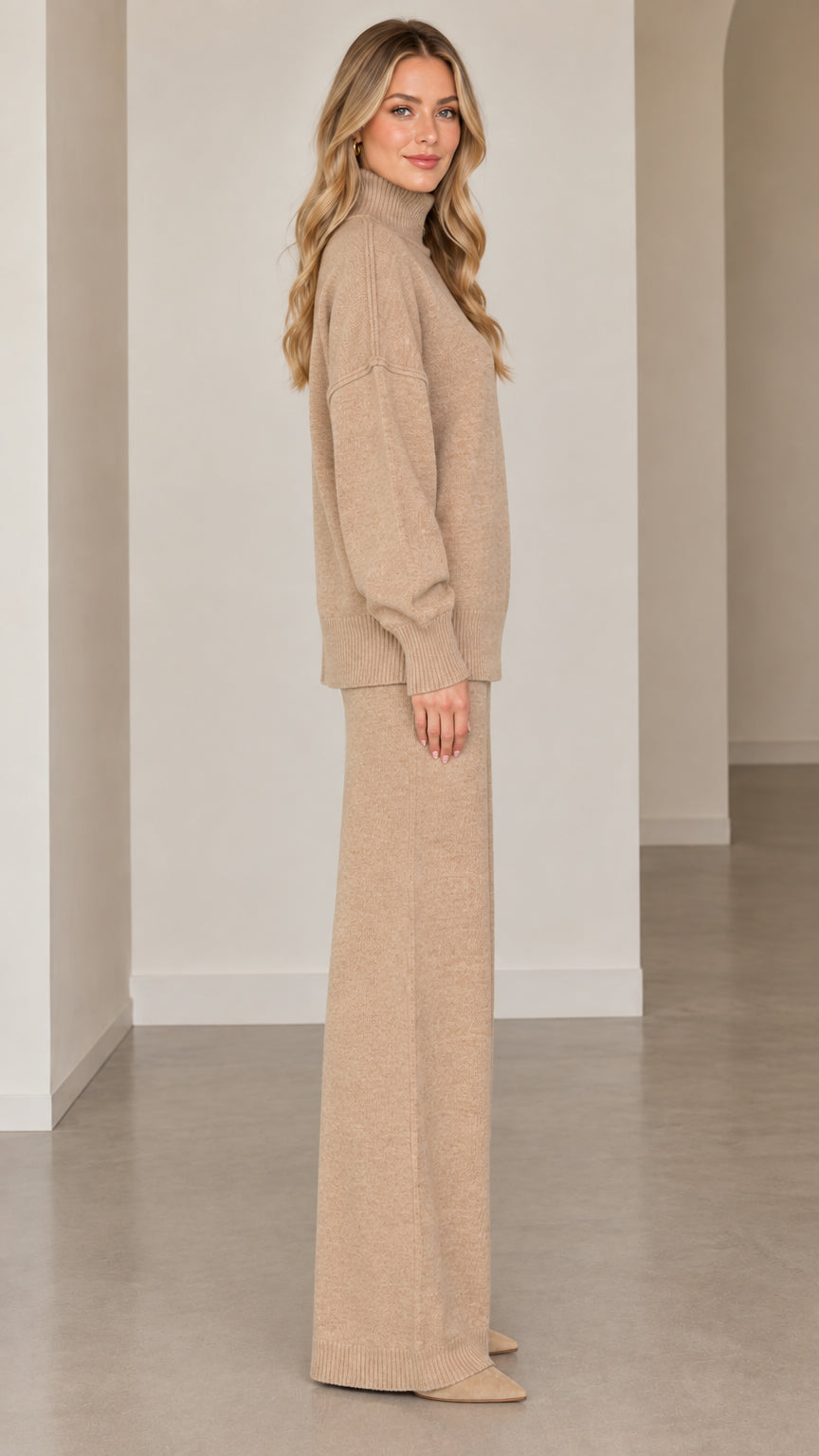 Side full-length view of model wearing beige knit turtleneck sweater and wide-leg trousers