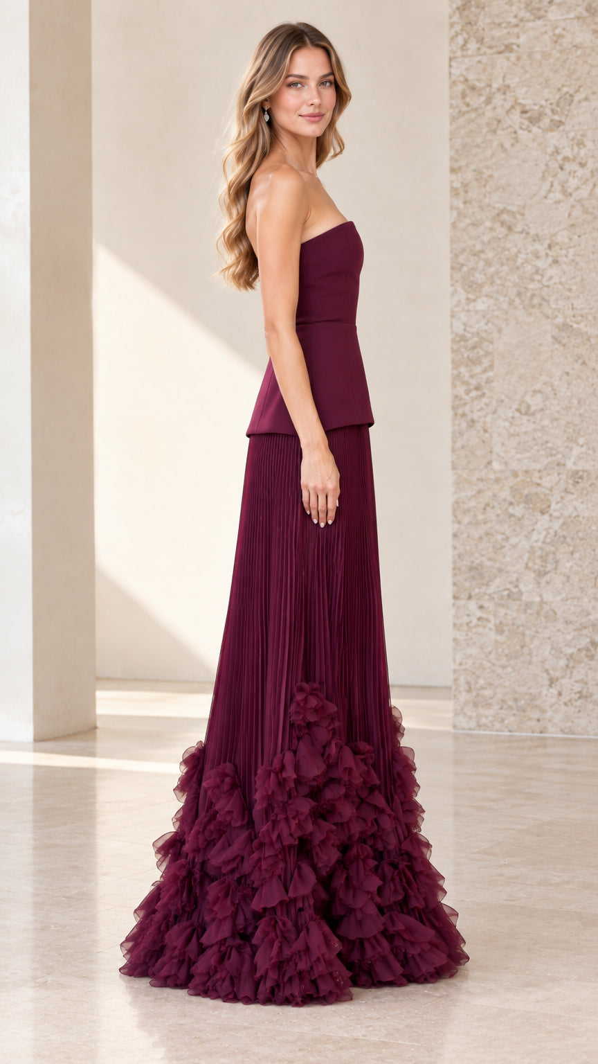 Side profile view of model wearing burgundy strapless peplum pleated evening dress