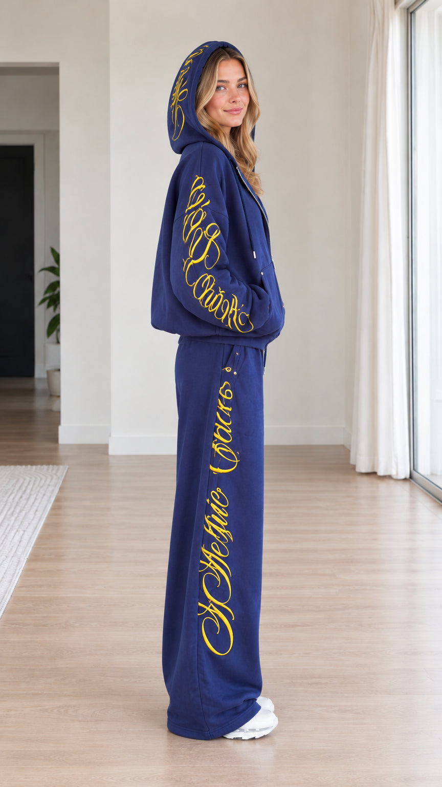 Side profile view of royal blue two-piece tracksuit showing script embroidery along the leg and sleeve
