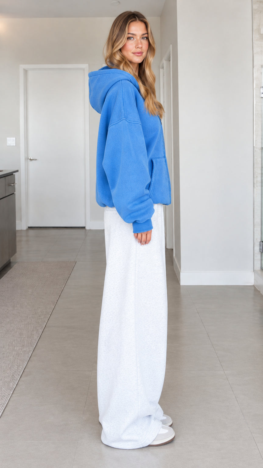 Side full-length view of a woman wearing a blue drop-shoulder zip hoodie with white wide-leg pants