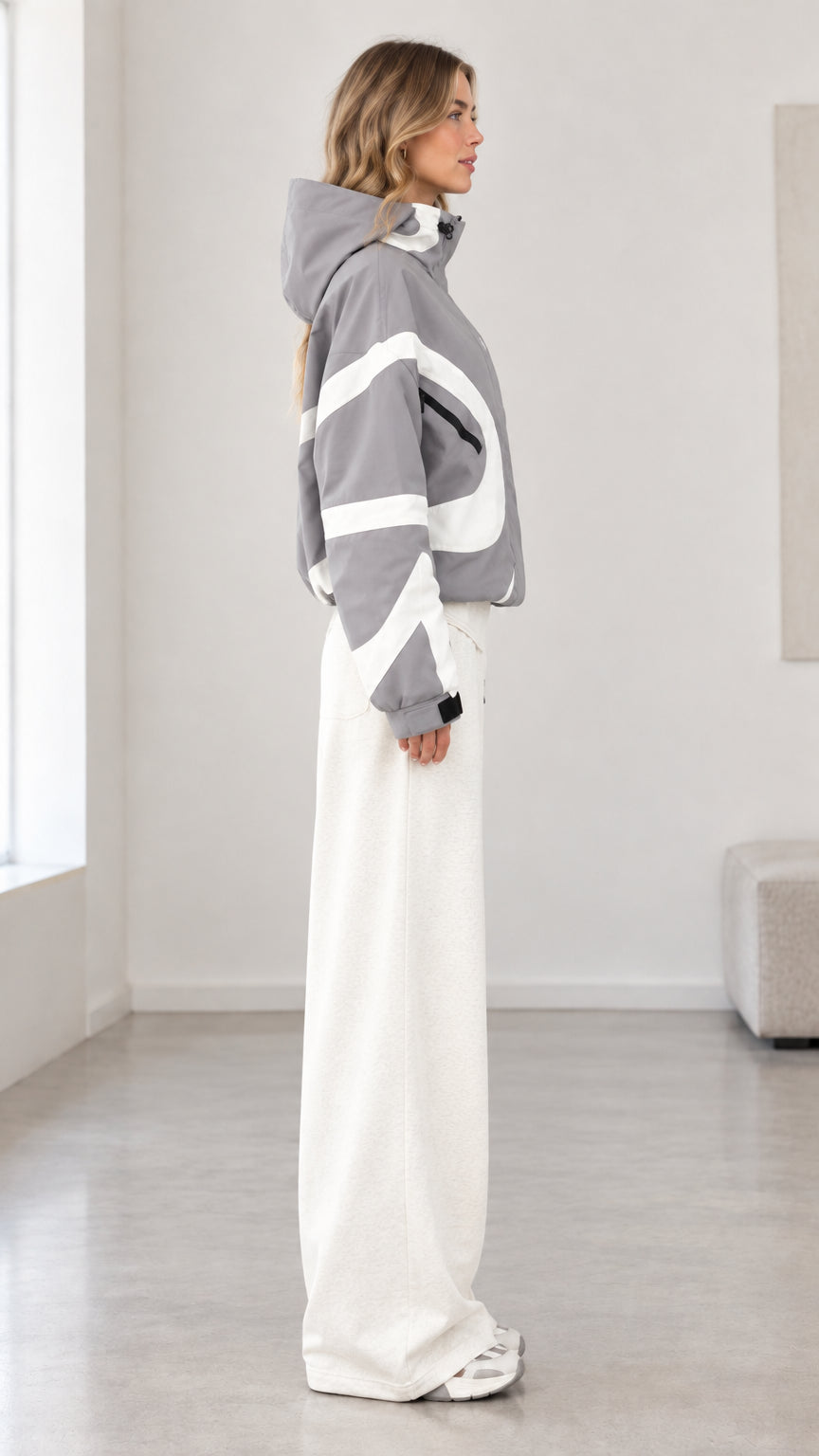 Side profile of model wearing grey hooded jacket showing sleeve wave paneling and profile fit