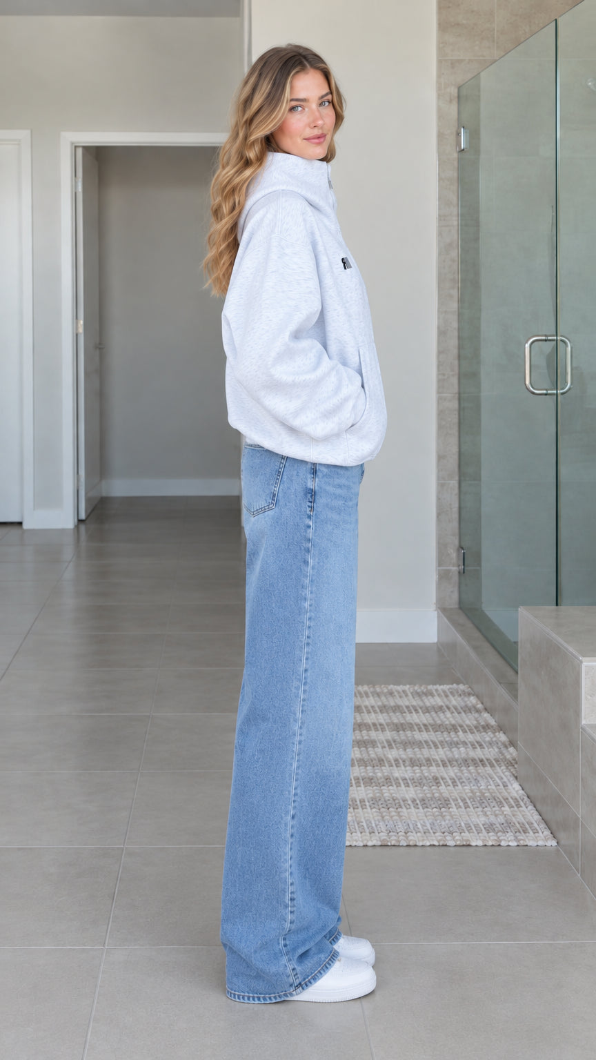 Side profile view of model wearing heather grey oversized zip-up hoodie jacket with wide leg denim jeans
